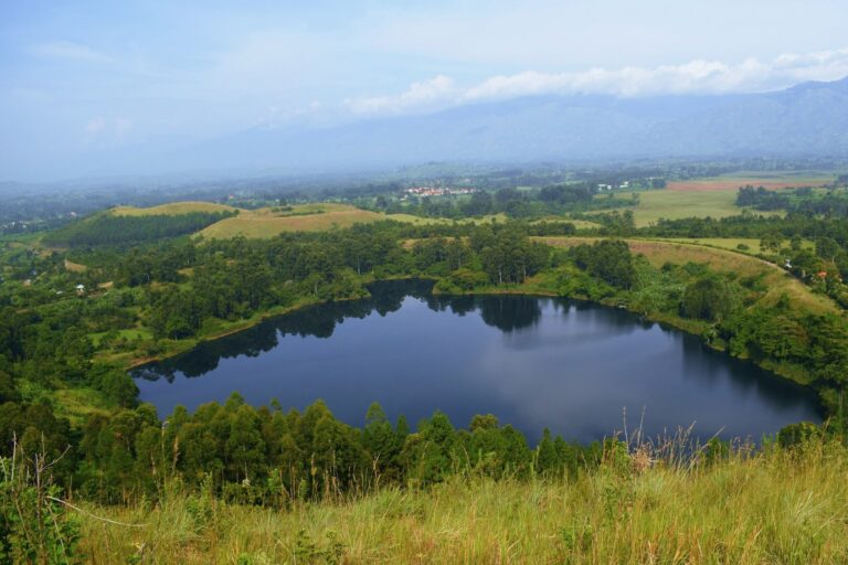 Deep blue crater lake among green hills near Fort Portal, western Uganda, with mountains beyond